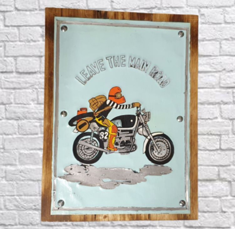 A wooden backboard with a painted tin front reading leave the Main Road with a motorbike and rider underneath