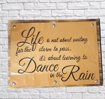 a wooden backboard with a painted and embossed front reading life is not for waiting for the storm to pass. It's about learning to dance in the rain