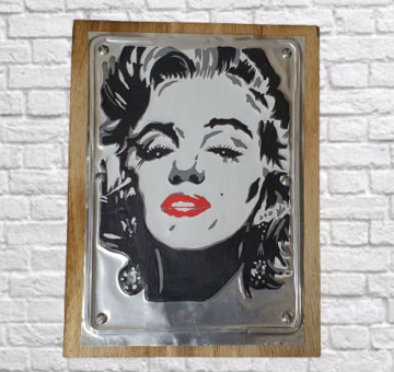 A wooden backboard with a tin embossed and painted front picture of Marilyn Monroe