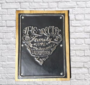 a wooden backboard with a tin embossed and painted front of a family moto. The recipe for family is simple, the only thing needed is unconditional love, all painted in black and white in the shape of a heart.