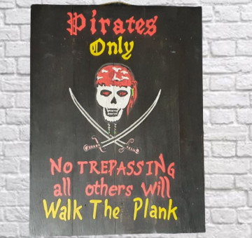 A wooden painted sign with black background, the wording of Pirates Only No Trepassing all other will walk the plank