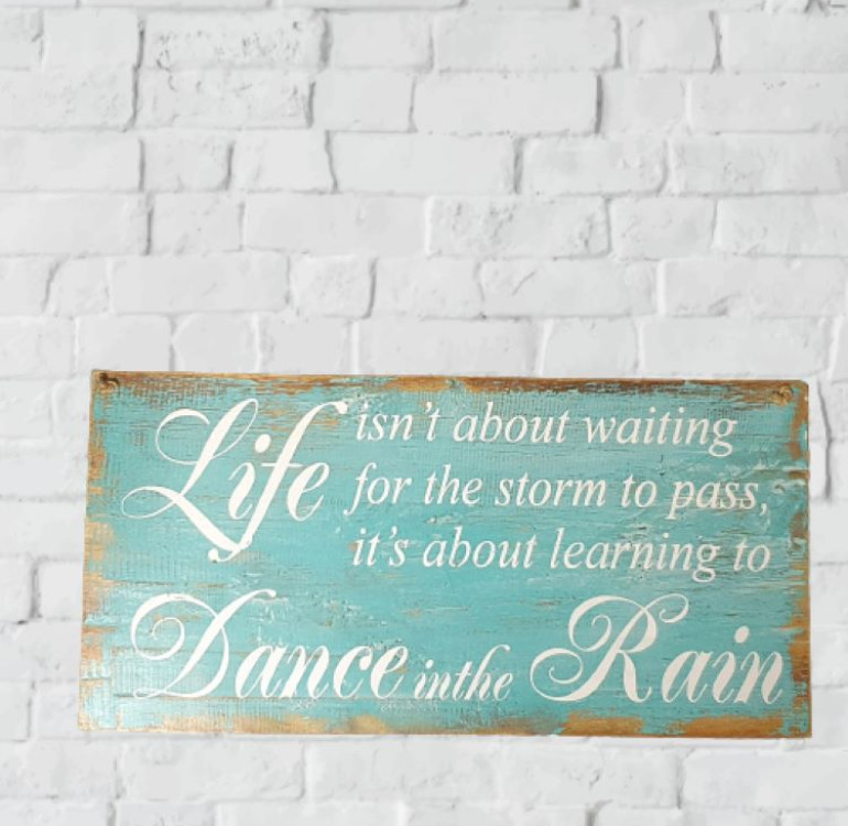 a wooden painted sign with the words Life isn't about waiting for the storm to pass it's about learning to Dance in the rain, coastal wind washed sign with twisted rope hanging