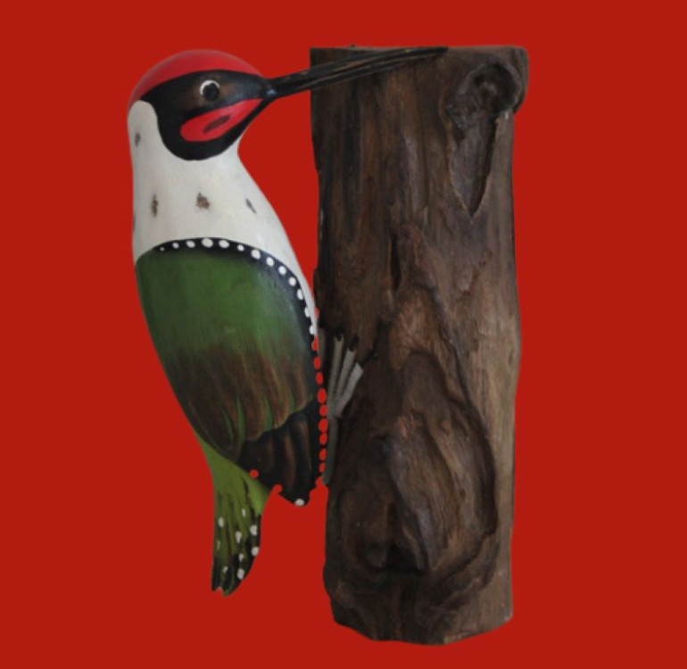 An image of a green hand painted hand carved wooden woodpecker hanging onto a unique piece of wood