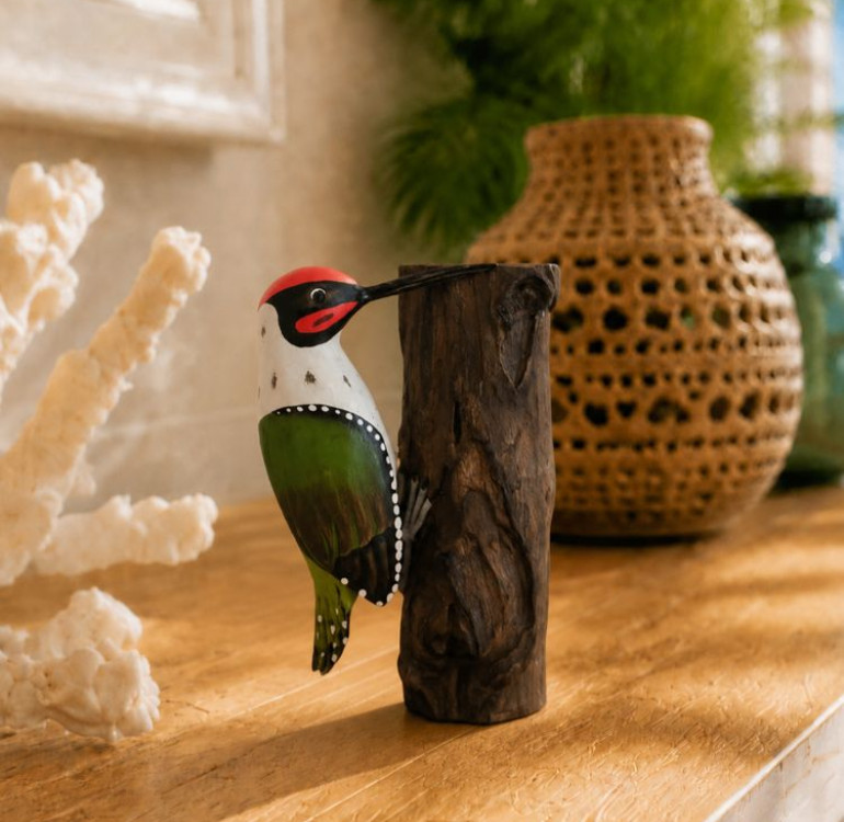 An image of a green hand painted hand carved wooden woodpecker hanging onto a unique piece of wood