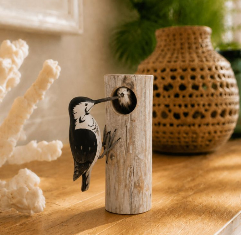 An image of a black and white wooden hand carved and hand painted woodpecker on wood with a baby peering through
