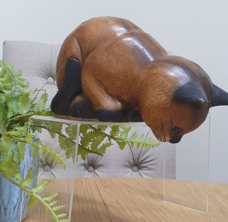 A hand carved sitting cat peering over the edge of a shelf