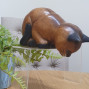 A hand carved sitting cat peering over the edge of a shelf
