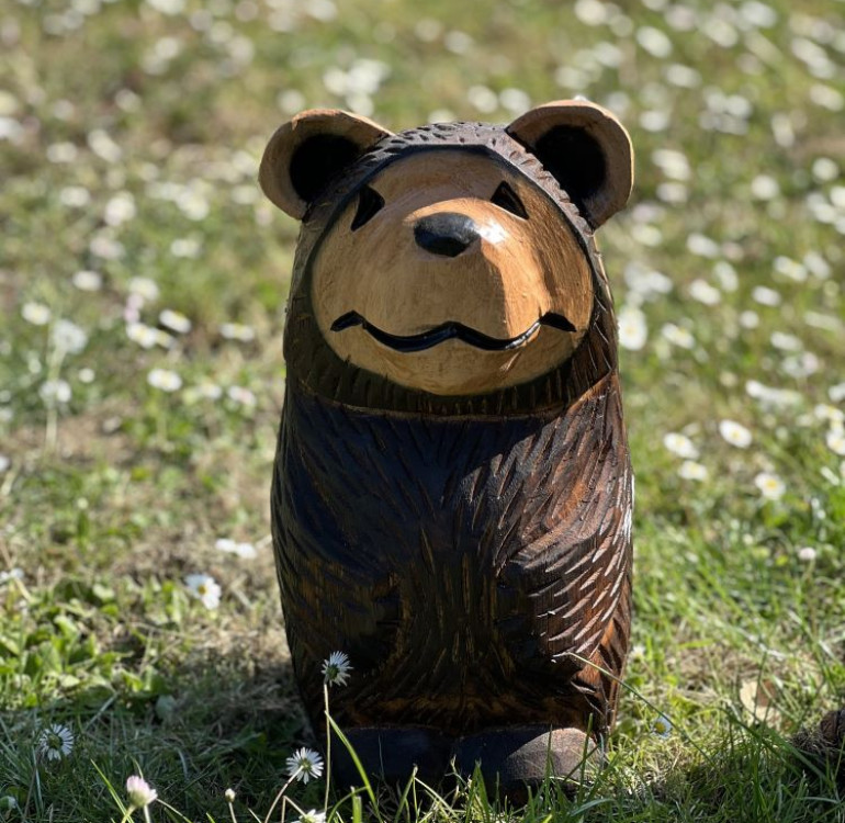 a hand carved outdoor wooden bear sculpture, tired squinty eyes
