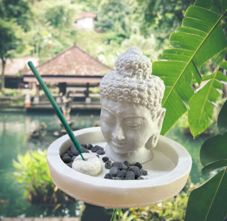 a white stone effect buddha on garden with incense sticks and candle